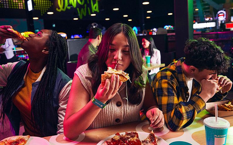 Three friends eating pizza, poutine, and a quesadilla.